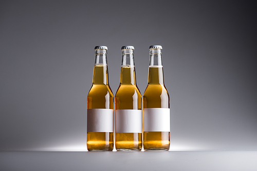 three glass bottles with beer and white labels in row on dark background