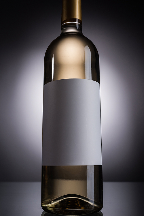 low angle view of bottle with white wine and blank label on dark background with back light