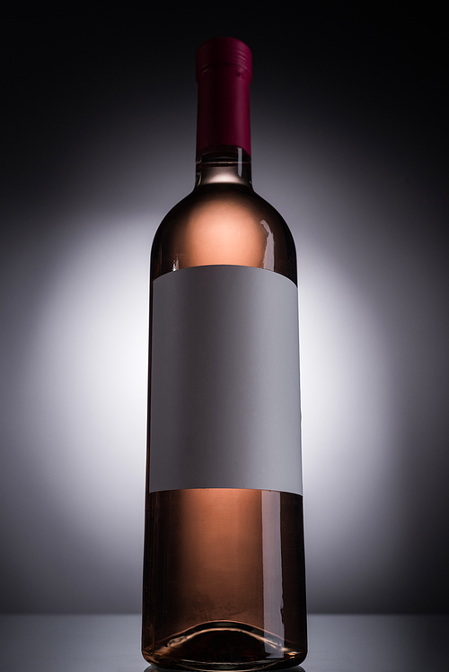 low angle view of bottle with rose wine and blank label on dark background with back light