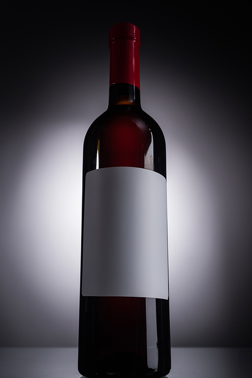 low angle view of bottle with red wine and blank label on dark background with back light