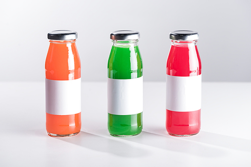 row of glass bottles with multicolored liquid and white labels isolated on grey