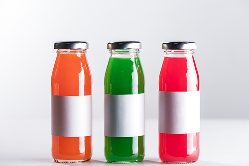 row of glass bottles with multicolored liquid and white blank labels isolated on grey