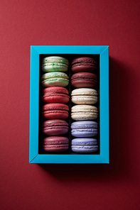 top view of assorted delicious colorful french macaroons in box on red background