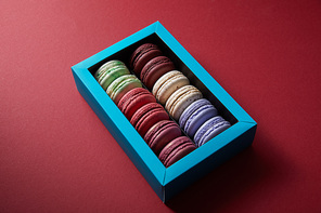 assorted delicious colorful french macaroons in box on red background