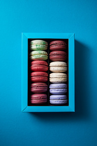 top view of assorted delicious colorful french macaroons in box on blue background