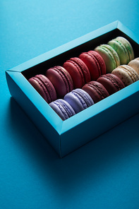 assorted delicious colorful french macaroons in box on blue background