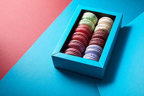 assorted delicious bitten colorful french macaroons in box on blue and red background