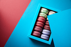 top view of assorted delicious bitten colorful french macaroons in box on blue and red background