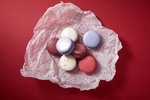 top view of assorted delicious colorful french macaroons on crumpled paper on red background