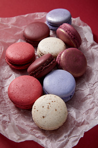 close up view of assorted delicious colorful french macaroons on crumpled paper on red background