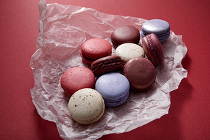 assorted delicious colorful french macaroons on crumpled paper on red background