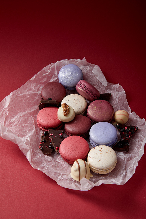 assorted delicious colorful french macaroons on crumpled paper with chocolate on red background