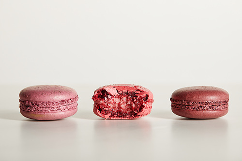 delicious whole and one bitten red french macaroons on white background
