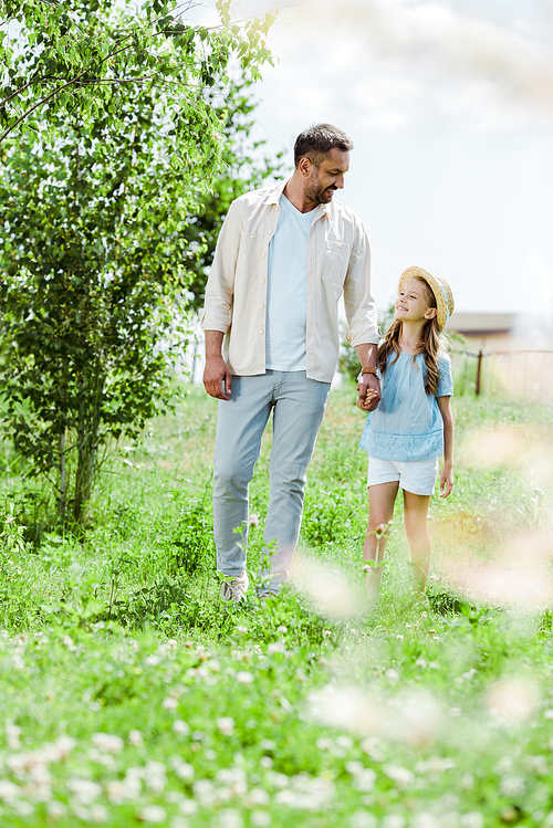 selective focus of father and daughter walking near green plants and holding hands