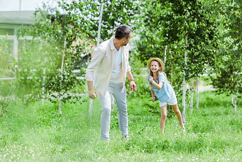 selective focus of happy kid gesturing while looking at father and standing on grass