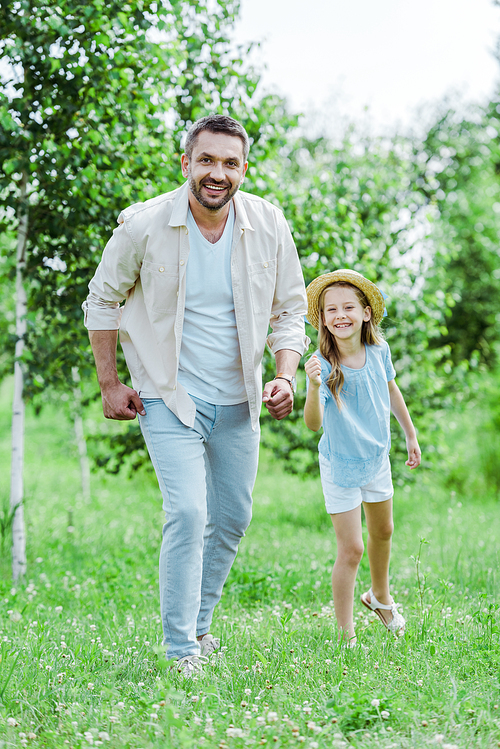 cute and happy kid in straw hat gesturing near cheerful father 