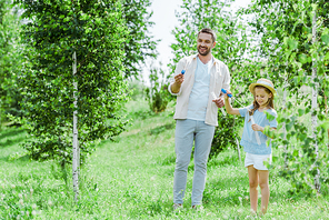 selective focus of cheerful father and daughter holding bubble wands while standing near trees