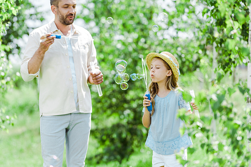 selective focus of cheerful father looking at daughter blowing soap bubbles