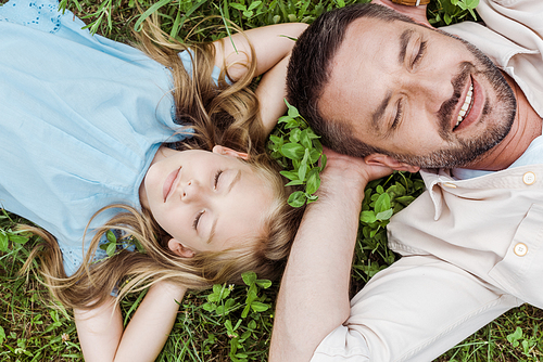 top view of happy father and daughter lying on green grass