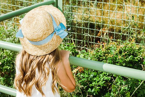 kid in straw hat standing near metallic cage in zoo