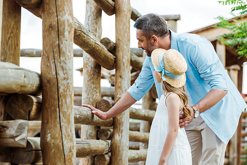 selective focus of handsome man standing near kid in straw hat and wooden fence in zoo