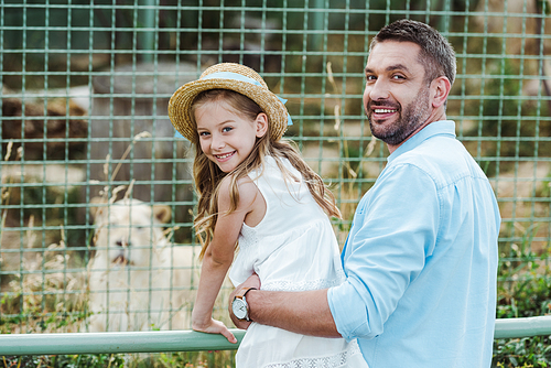 happy dad and daughter  near cage with wild animal in zoo