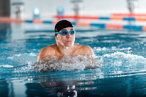 selective focus of handsome athletic man in goggles and swimming cap in swimming pool