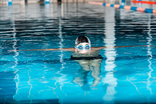 cropped view of swimmer in swimming cap and googles in water
