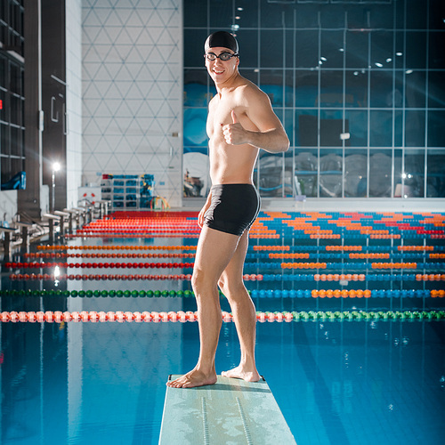 smiling swimmer showing thumb up while standing on diving board