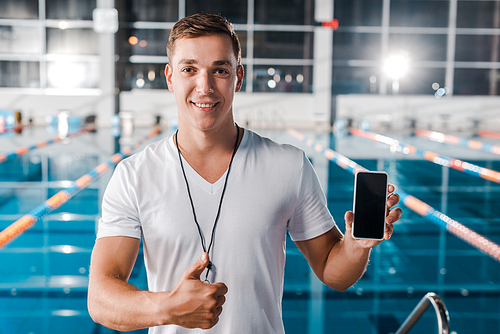 happy trainer showing thumb up while holding smartphone with blank screen
