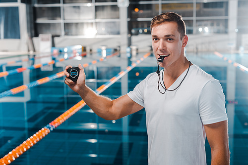 smiling trainer with timer in hand holding whistle in mouth