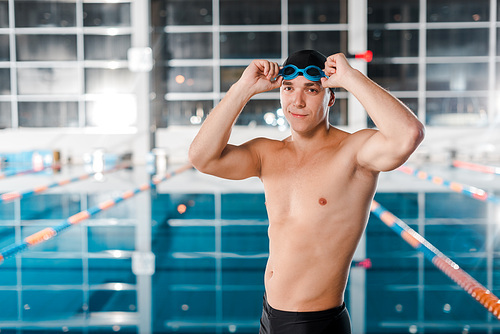 happy athletic swimmer touching goggles near swimming pool