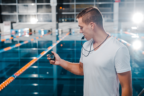 trainer in white t-shirt looking at timer while holding whistle in mouth