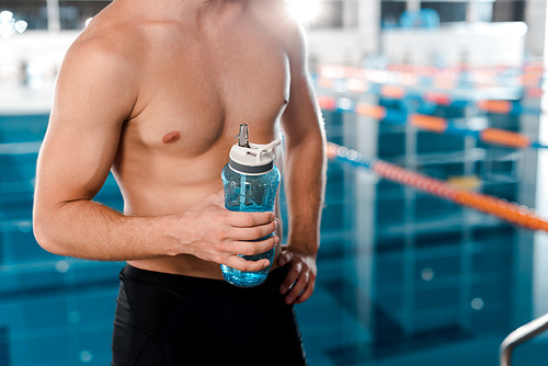 cropped view of muscular sportsman holding sports bottle near swimming pool