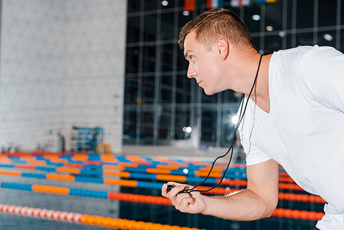 side view of trainer holding timer and looking at swimming pool