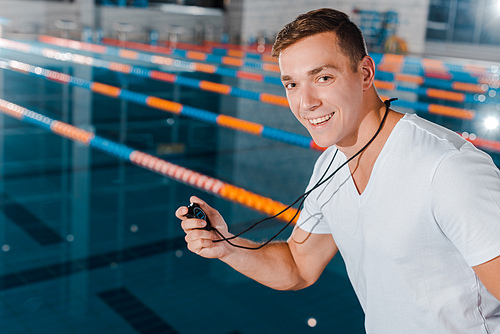 cheerful trainer holding timer and  near swimming pool