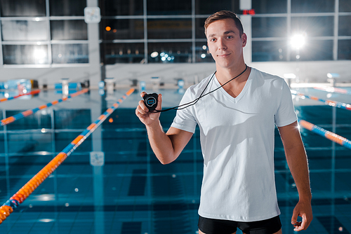 handsome trainer holding timer and  near swimming pool