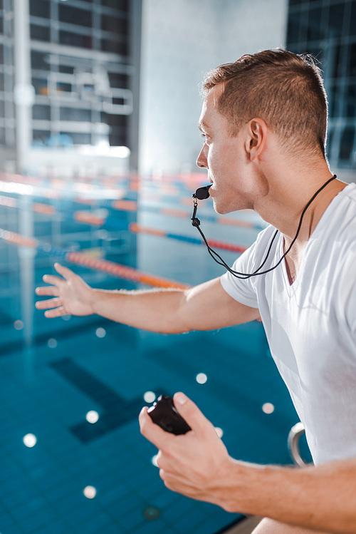 selective focus of trainer with whistle in mouth gesturing while holding timer