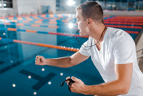 emotional trainer with whistle in mouth gesturing while looking at swimming pool