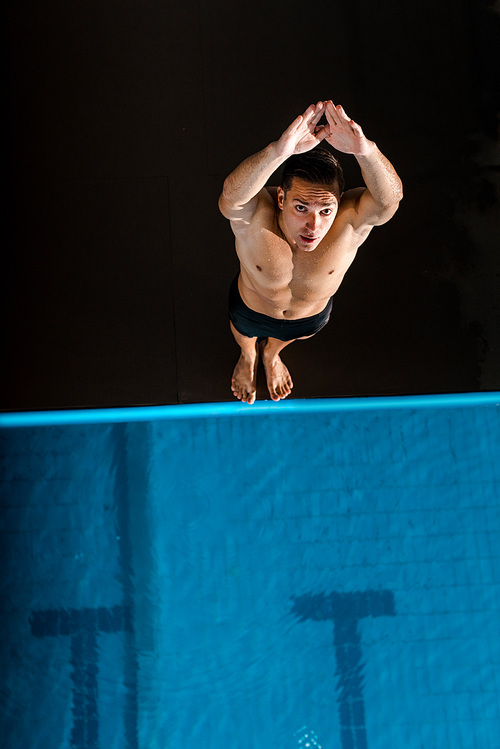 top view of handsome swimmer standing with outstretched hands near swimming pool