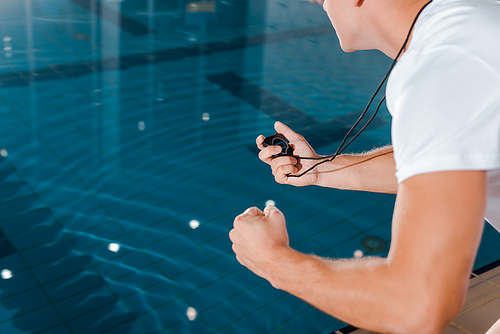 cropped view of athletic trainer with timer near swimming pool