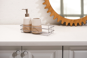 Dispenser liquid soap, toothbrush holder on shelf near round mirror on wall in bathroom, zero waste concept