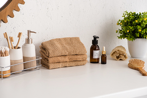 Shelf with hygiene objects near towels, beauty products and flowerpot in bathroom, zero waste concept