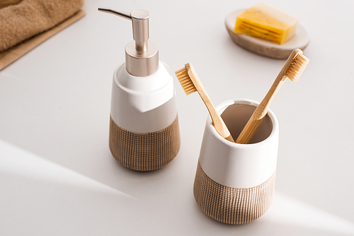 Close up view of liquid soap, toothbrush holder with toothbrushes, towels and dish with soap on grey, zero waste concept