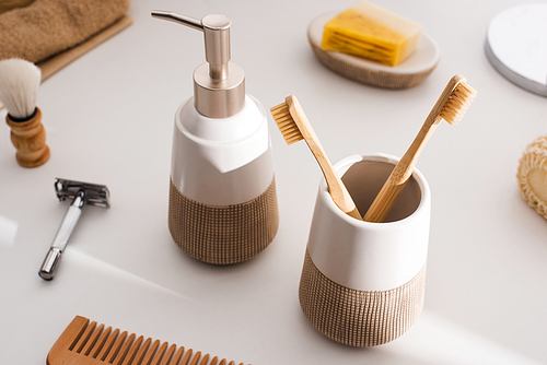 Close up view of liquid soap, toothbrush holder with toothbrushes and hygiene objects on grey, zero waste concept