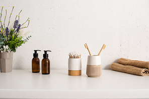 Flowerpot, eco body cream, toothbrush holders with hygiene objects and towels in bathroom, zero waste concept