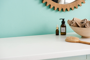 Hairbrush, bottles of eco body cream and oil, bowl with towels near mirror in bathroom, zero waste concept