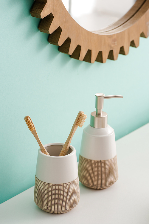 Toothbrush holder with toothbrushes and liquid soap near round mirror on wall in bathroom, zero waste concept