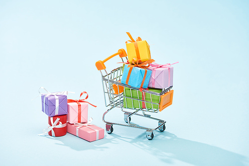 festive wrapped gifts in shopping cart on blue background