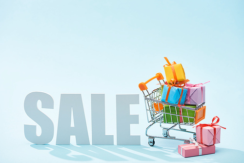 white sale lettering and festive gift boxes in shopping cart on blue background